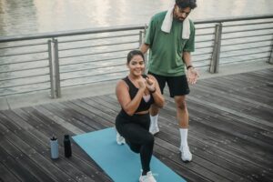 Man and woman exercising by a riverside, focused on lunges and fitness training.