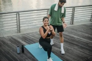 Man and woman exercising by a riverside, focused on lunges and fitness training.